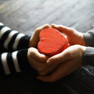 Hands of a woman holding and offering a heart shape.